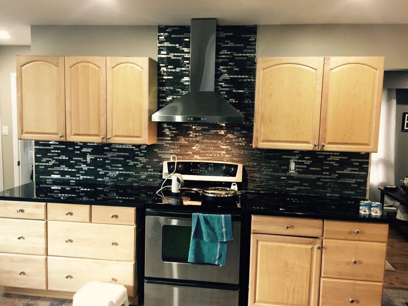 Kitchen with maple cabinets, a black glass-mosaic backsplash and a stainless range hood