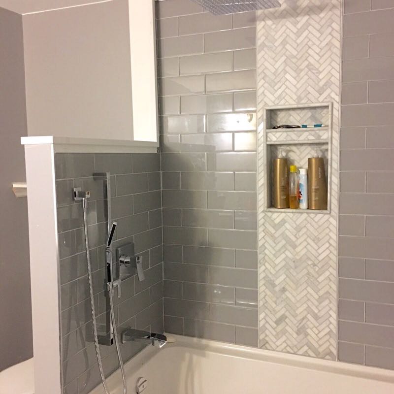 Tub and shower in grey subway tile with a herringbone mosaic strip and a recessed niche