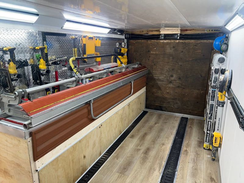 Inside the trailer looking toward the back, with a long bench and racked tools